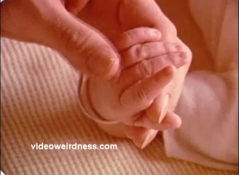 The still from the 'Red Cross PSA' features a close-up of an adult hand gently holding a small child's hand. The hands are clasped together, symbolizing care and support. The background appears soft and neutral, emphasizing the tender moment between the two. This imagery likely conveys a message of compassion and protection, central themes of the Red Cross mission.