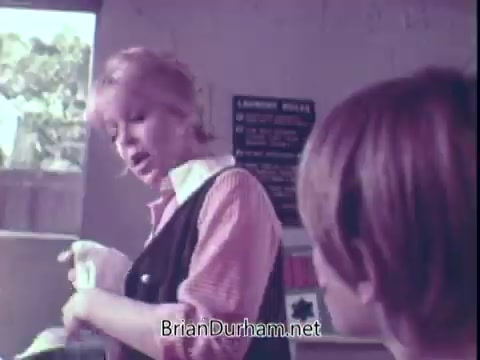 The still features a woman with light hair, wearing a sleeveless black top over a striped shirt, engaging with a young boy. They are in a bright setting, likely a home, with sunlight filtering through a window. The woman appears to be demonstrating or explaining something related to laundry, possibly the use of Biz laundry detergent, which is the focus of the commercial. The overall tone seems conversational and instructional.
