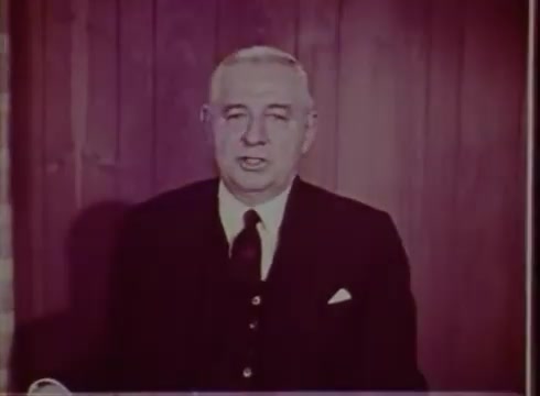 The still from the 1961 film 'Pres of Bell Tell of PA' features a man in a formal black suit with a white pocket square, sitting in front of a wooden backdrop. He appears to be delivering a message or outro for the film, which was sponsored by Bell Telephone of Pennsylvania. The overall tone is professional, indicative of corporate communication from that era.