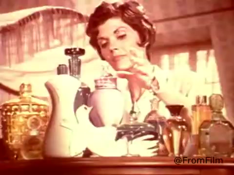In this 16mm still from a 1970s Dove dishwashing detergent ad, a woman is seen in a bright, well-lit kitchen setting. She is engaging with a collection of elegant bottles and containers, including a prominent Dove product that resembles a decorative ceramic dove. The soft color palette and nostalgic aesthetic emphasize the ad's theme of Dove as a gentle, moisturizing detergent, likened to a hand lotion. The playful tagline, “Stand back, madam - Dove is the dishwashing detergent that thinks it's a hand lotion!” captures the essence of the product's unique positioning.    for more vintage insights!