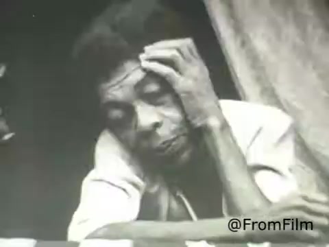 The still from the 1969 PSA by the American Institute of Architects features a reflective figure, likely deep in thought or contemplation. The monochromatic tones enhance the emotional weight of the image, evoking a sense of introspection. The simplicity of the scene contrasts with the complexities of architectural themes being addressed in the PSA, highlighting personal experience within the broader context of societal issues.