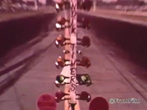 The still captures a moment from a 1960s drag race featuring a staging light tree, which is essential for starting the race. The lighting structure indicates the race procedure as drivers prepare to compete. The context of the voice-over highlights Don Garlits, a notable drag racer discussing car maintenance and performance, underscoring the importance of having a vehicle in optimal condition for racing success.   For the Dodge mentioned, if the image were present, identifying the specific model year would depend on visual cues like design features, but specific identification cannot be made without more details. The focus is on racing techniques and vehicle maintenance rather than the specifics of any one car.