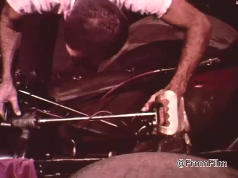 In the still from 'Dragsters and Cars,' the scene depicts Don Garlits, a renowned drag racer, as he engages in car maintenance. He is focused on the inner workings of a race car, emphasizing the importance of keeping the vehicle in optimal condition for competitive drag racing. The image captures the hands-on nature of his work, highlighting the mechanical aspects and the rigors of maintaining a high-performance car.   As for the specific year of the Dodge mentioned, additional context or knowledge about the model or visual details would be necessary to provide an accurate identification.