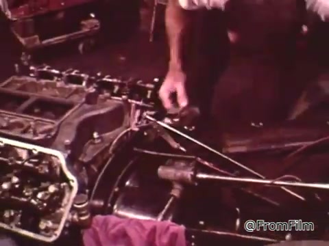 The still from the 16mm film 'Dragsters and Cars' features a close-up of car maintenance, likely focusing on an engine component. A hand is seen working on the parts, representing the meticulous care required for racing vehicles.   As for the year of the Dodge in the context given, it may be associated with the 1960s, considering the film's focus on that era's drag racing scene. Specific identification of the model would require more details or visual context.