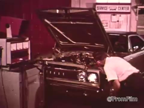 The still from 'Dragsters and Cars' features a mechanic working on a Dodge vehicle, likely from the late 1960s. The scene emphasizes car maintenance, with an emphasis on performance. The context suggests that maintaining a car in peak condition is crucial for success in drag racing, as highlighted by Don Garlits in the voice-over. The Dodge's specific model year isn't identifiable from the image alone, but it likely falls within that era.