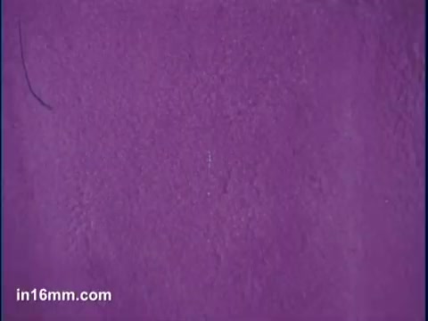 The still features a textured surface predominantly in a vibrant purple hue. The focus appears to be on the color's richness, likely emphasizing the dye's intensity. The simplicity of the background suggests a creative approach, possibly showcasing the dye's application or effect in a tie-dye context.