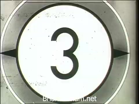 The still features a countdown graphic, typically seen in classic film or video presentations. It indicates the number '3' within a circular frame, reminiscent of mid-20th century cinema. This piece is likely promoting electric water heaters by the Wheeling Electric Company, humorously comparing them to a friendly puppy for their convenience and proximity to home appliances. The context suggests a playful, nostalgic approach to advertising, capturing mid-century marketing aesthetics.