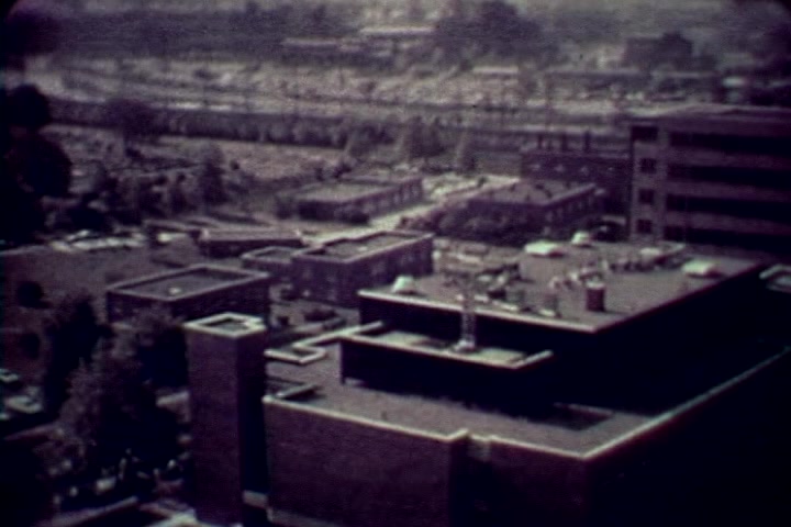 The still depicts an aerial view of a cityscape, likely Philadelphia, featuring rooftops of various buildings with a focus on urban structures. The surrounding area shows a mix of industrial and residential components with a distant skyline, reflecting the environment of the 1970s. The muted colors suggest the film's aged 16mm quality, contributing to the somber tone typical of anti-drug narratives during that era. The imagery serves as a backdrop to the documentary’s serious themes regarding drug abuse.