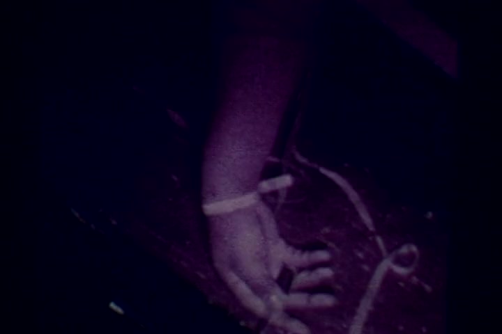 The still from the anti-drug film 'Drug Abuse: Some Comments from the Morgue' shows a close-up of a hand resting on a surface, highlighted in a somber color palette. The image conveys a stark message about the consequences of drug abuse, likely illustrating a scene related to overdose or its aftermath. The context suggests a serious tone aimed at raising awareness about the dangers and repercussions of drug use during the 1970s.
