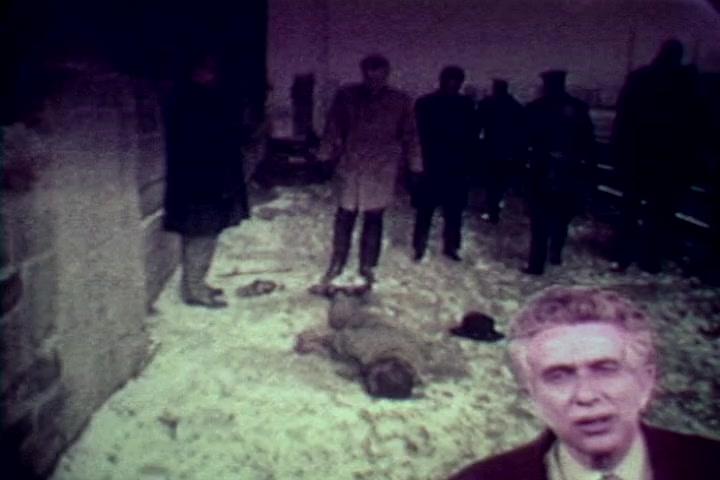 The still from 'Drug Abuse: Some Comments from the Morgue' depicts a grim scene in a snowy urban environment. In the foreground, a man, likely Tillman Hahn, speaks directly to the camera, conveying a serious message. Behind him, a body lies on the ground, surrounded by several individuals, including law enforcement and bystanders, observing the situation. The overall tone is somber and reflects the film's anti-drug narrative, illustrating the stark realities of drug abuse's impact.