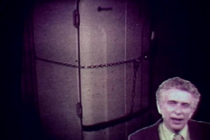 The still features a dimly lit morgue scene, highlighting a locked, chain-bound refrigerator, which likely serves to store bodies. In the foreground, Tillman Hahn, a representative from the Medical Examiner's office, is speaking directly to the camera. His serious demeanor underscores the grim context of the film, which aims to address the harsh realities and consequences of drug abuse. The overall tone is somber, reflecting the film's anti-drug message from the 1970s.