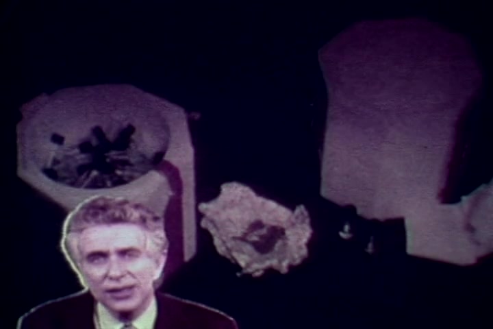 The still features Tillman Hahn speaking directly to the camera, likely addressing the audience about the dangers of drug abuse. In the background, there are shadowy, indistinct objects that may represent drug paraphernalia or evidence from drug-related incidents. The color palette suggests a vintage look typical of 1970s films, enhancing the serious tone of the anti-drug message being conveyed.