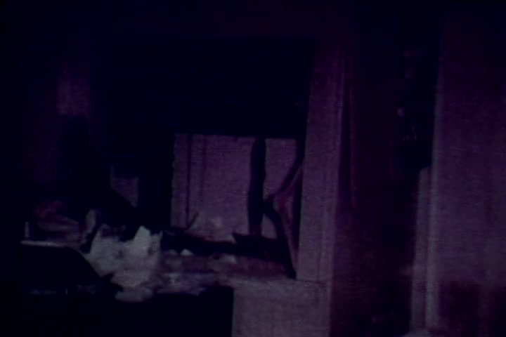 The still from 'Drug Abuse: Some Comments from the Morgue' presents a dimly lit, unsettling scene, likely from a morgue environment. It features disorganized clutter, suggesting an atmosphere of neglect and decay, typical of drug-related death. The focus is on shadows and muted colors, evoking a sense of somber reflection on the consequences of drug abuse, consistent with the film's anti-drug message.