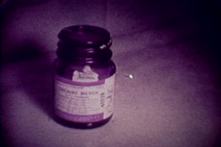 The still features a close-up of a purple glass jar, likely a pharmaceutical container. The label includes text indicating its contents, which may relate to drugs or medication. The background appears muted and somewhat subdued, typical of the film's 1970s aesthetic. This image likely serves as a visual reference to substance abuse and its consequences, fitting the film's anti-drug theme.