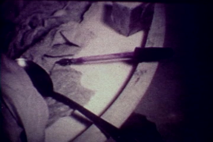 The still from 'Drug Abuse: Some Comments from the Morgue' features a close-up of a spoon and a syringe resting on a circular surface. The setting is dimly lit, emphasizing the somber context of drug use. The spoon appears to be stained and possibly used for drug preparation, while the syringe suggests the act of injection. The overall composition conveys a stark message about the dangers of drug abuse, reflecting the film's anti-drug themes from the 1970s.