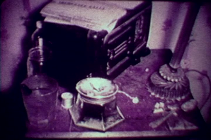 The still from 'Drug Abuse: Some Comments from the Morgue' features a cluttered tabletop scene, likely depicting items associated with drug use. A drink glass, a paper-covered object, and metal spoons are visible, suggesting a casual or domestic setting. The overall tone is somber, reflective of the film's anti-drug message from the 1970s. The muted colors and vintage look reinforce the era's aesthetic, emphasizing the gravity of drug abuse.
