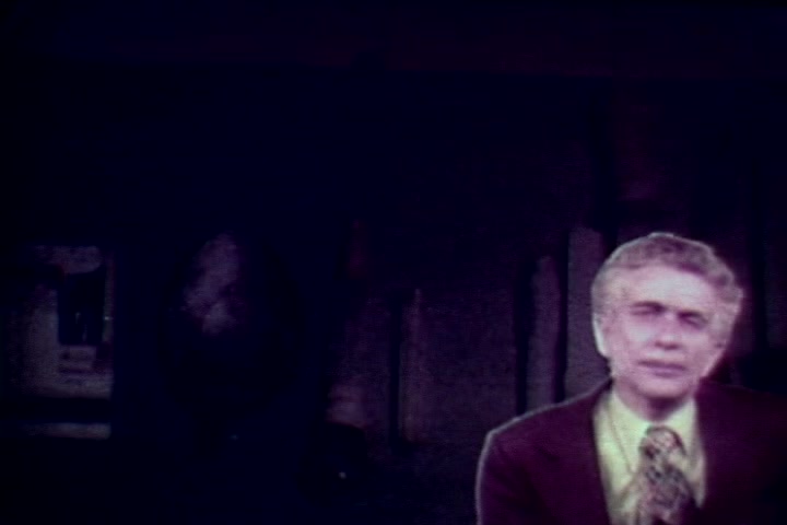 The still features a seated individual, likely Tillman Hahn, in a suit and tie, speaking directly to the camera. The background is dimly lit, suggesting a serious atmosphere, possibly reflecting themes of mortality and the impact of drug abuse. The image appears somewhat muted, typical of 16mm film, enhancing its somber tone in this anti-drug context from the 1970s.