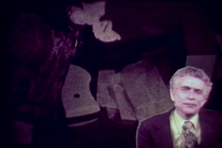 The still appears to depict a somber scene from the anti-drug film *Drug Abuse: Some Comments from the Morgue*. In the foreground, an individual—likely Tillman Hahn—speaks directly to the camera, dressed in a suit. The background features a shadowy figure and potentially morbid imagery associated with drug abuse, reflective of the film's grave subject matter. The colors are muted, characteristic of 1970s film print, creating a serious tone that underscores the film's anti-drug message.