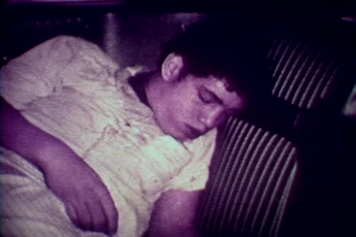 The still features a young man slumped in a seated position, appearing unresponsive. He is dressed in a light-colored shirt, and the setting suggests a somber environment typical of a medical or morgue context. The image captures a stark, distressing moment, emblematic of the film's anti-drug message and the tragic consequences of substance abuse. The muted colors and graininess of the 16mm print reflect the era's documentary style, enhancing the film's serious tone.