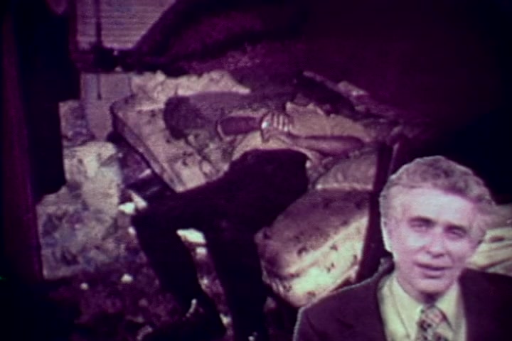 The still from 'Drug Abuse: Some Comments from the Morgue' depicts a somber scene with a deceased individual slumped on a disheveled couch, surrounded by a cluttered room. In the foreground, Tillman Hahn from the Medical Examiner's office appears, likely providing commentary on the implications of drug use. The overall tone is grim, highlighting the stark realities of substance abuse in the 1970s. The film aims to convey a strong anti-drug message through its stark imagery and informative narration.