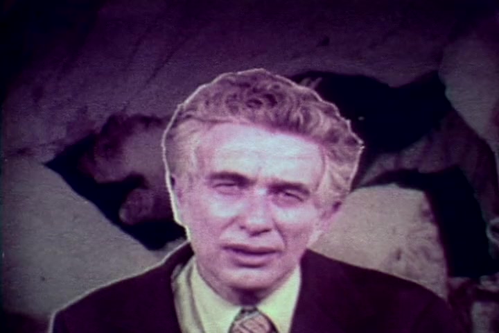 The still features Tillman Hahn from the Medical Examiner's office, appearing somber and concerned. He is in the foreground, addressing the camera, while the blurred background suggests a morgue setting, reinforcing the film's grim anti-drug message. The lighting and color give a vintage feel typical of 1970s educational films, emphasizing the serious nature of the topic.