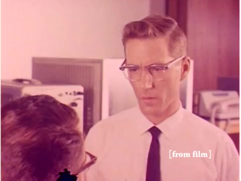The still depicts two men engaged in conversation, likely in a professional or engineering context, given the film's theme. One man, wearing glasses and dressed in a white shirt and tie, appears to be listening intently, showcasing a serious expression. The surroundings suggest a laboratory or office environment, possibly filled with older computer equipment in the background. The film, from 1967, focuses on topics such as preventing data transmission errors using technology from that era. The visible lab defect adds an interesting layer to the vintage feel of the footage.