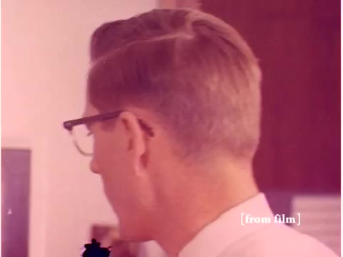 The still from 'Bell System - Preventing Data Transmission Errors' features a man with a side-parted hairstyle seen from the back and side. He wears glasses and a collared shirt, and the scene suggests a professional environment, likely an engineering or computing lab. The image has a faded quality typical of older films, hinting at the vintage nature of the 1967 footage. Given the film's theme, this moment likely captures an engineer engaged in work related to data transmission, amidst the technological context of the era. The lab defect adds an additional layer of historical character to the visual.