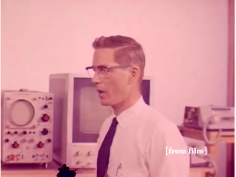 The still features a man in a white shirt and tie, wearing glasses, standing in a lab-like environment. Behind him are electronic devices, including an oscilloscope and what appears to be an early computer monitor. The setting conveys a mid-20th century technological atmosphere, typical of a Bell System production from 1967. The scene likely focuses on data transmission error prevention, with an emphasis on the tools and personnel involved in the process. The image was captured from a silent negative, indicating some film defect, which may affect clarity or color.