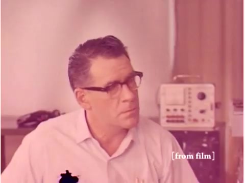 The still from the 1967 Bell System film depicts an engineer with glasses, appearing to contemplate or discuss something. The background features an oscilloscope and other lab equipment typical of the era. The image suffers from a lab defect, resulting in unusual coloration and markings. This film focuses on preventing data transmission errors, showcasing various technologies like computers and acoustic modems.