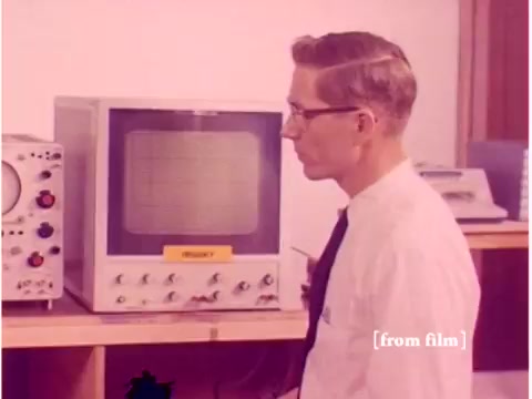 The still features a male engineer wearing glasses, observing an oscilloscope, which is a piece of test equipment widely used in electronics. The oscilloscope is positioned on a shelf alongside several other devices, likely related to telecommunications. The setting appears to be a laboratory, indicative of a technical environment. The image reflects the early era of computing and data transmission, highlighting the tools used to prevent data transmission errors during that time. The film itself is noted to have defects, which adds a layer of historical authenticity.