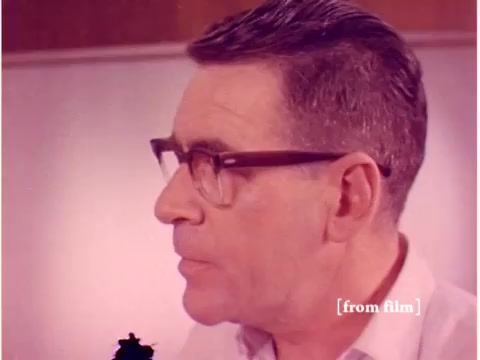 The still features a man with short, neatly combed hair, wearing glasses and a light-colored shirt. He is facing to the right, with a serious expression, likely engaged in a discussion or analysis related to the film's topic on preventing data transmission errors. The background is subtly blurred, suggesting a professional environment, possibly a lab or office setting. Given the context, the image may highlight the human element behind technological advancements in data transmission during the 1960s.