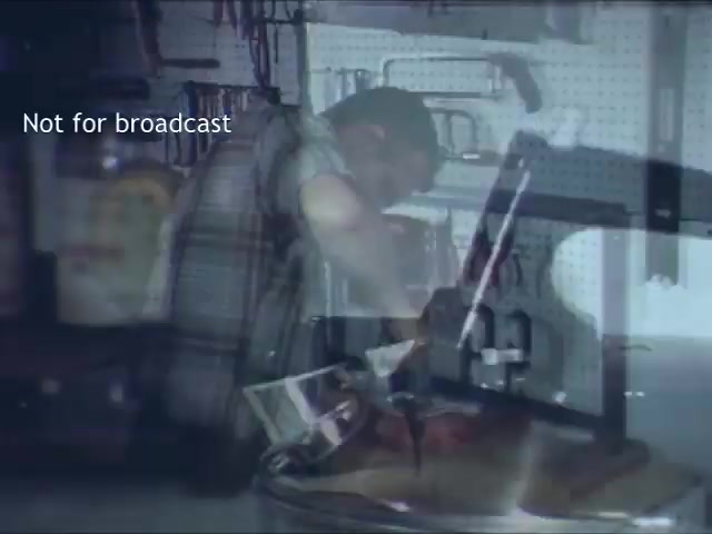 The still from the 'Bell Trimline Extension - C&P telephone commercial' features a person in a workshop setting, appearing to work intently on a project. The environment is cluttered with tools and equipment, suggesting a hands-on, DIY atmosphere. The overall focus is on the craftsmanship and utility, which aligns with promoting the Bell Trimline telephone's features. The overlay stating 'Not for broadcast' indicates it's a private or archival image, not intended for public viewing.