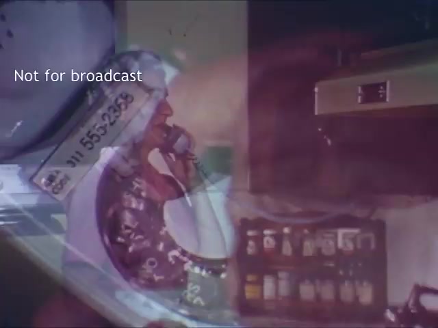 The still from the 'Bell Trimline Extension - C&P telephone commercial' features a person on the phone, showcasing the phone's design and functionality. The scene appears to be set in a kitchen, with various items visible in the background, hinting at a domestic environment. The focus on the phone indicates its appeal for convenient communication in everyday settings. It conveys a sense of modernity and accessibility associated with the Bell Trimline model. The overlay text indicates the image is not for broadcast.