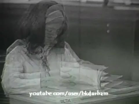 The still captures a young girl, presumably a sixth grader, sitting at a desk while focused on her schoolwork. The image has a monochrome, slightly blurred quality reminiscent of kinescope films from the era. She appears to be writing or reading from a textbook, highlighting a typical educational setting of the 1960s. The film’s purpose seems to align with teaching linguistic concepts in a classroom environment.