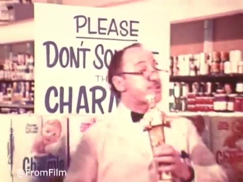 The still features a humorous scene from a vintage Charmin commercial featuring Mr. Whipple. He stands in front of a sign that reads 'PLEASE DON'T SQUEEZE THE CHARMIN!' while holding a product. The setting appears to be a grocery store, emphasizing the playful nature of the ad. The 16mm print captures the nostalgic quality of classic advertising.   Follow us on Twitter @FromFilm.