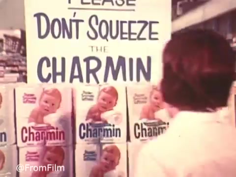 The still captures a classic moment from the Charmin commercial featuring Mr. Whipple. It shows a grocery store aisle with boxes of Charmin toilet paper prominently displayed. A sign reading 'PLEASE DON'T SQUEEZE THE CHARMIN' is prominently featured above the products. The playful tone highlights the humorous warning against squeezing the soft, gentle tissue, showcasing the brand's advertising charm.   Follow us on Twitter @FromFilm.