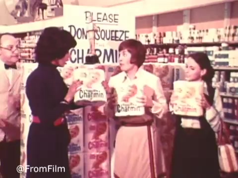 A still from the classic Charmin commercial featuring Mr. Whipple. The scene is set in a grocery store, with two women holding packages of Charmin toilet paper. One woman is dressed in a white apron while the other wears a black outfit. The iconic phrase 'Don't squeeze the Charmin!' is humorously reinforced as Mr. Whipple watches nearby, embodying the brand's playful approach to advertising. The vibrant colors and retro aesthetic of the 16mm print evoke nostalgia for vintage commercials.