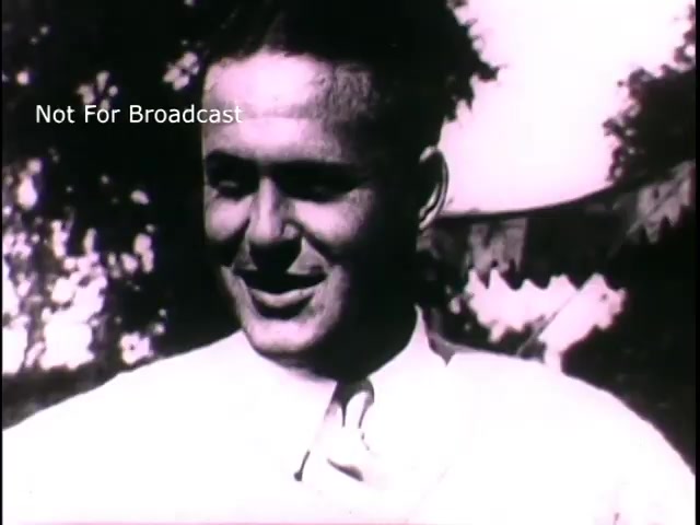 The still from 'US Army recruiting - 'Join the new action army'' depicts a smiling young man in a light-colored shirt, conveying a sense of optimism and engagement. The background features out-of-focus shapes that suggest a festive atmosphere, possibly indicating a community or recruitment event. This imagery reflects the 1960s recruitment efforts aimed at appealing to youth and promoting service in the Army. The overall tone is inviting and motivational.