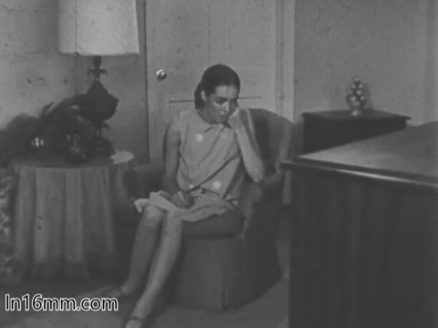 The still depicts a young girl sitting alone in a modest living room, appearing contemplative or sad. She is dressed in a simple dress and is seated in a chair, with a small table and lamp beside her. The overall atmosphere conveys a sense of seriousness, reflecting the theme of the March of Dimes campaign on birth defects.