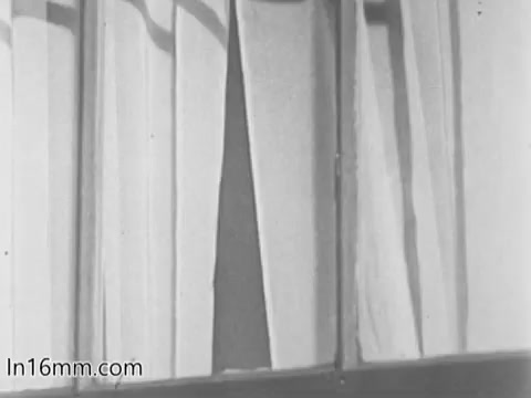 The still from the 'March of Dimes Birth Defects PSA' shows a close-up of window curtains, partially drawn, allowing a glimpse of the outside. The lighting appears soft, creating a calm atmosphere. This imagery likely sets the tone for the public service announcement's message regarding birth defects and their impact. The focus on the curtains may symbolize anticipation or a glimpse into a broader theme of hope and awareness.