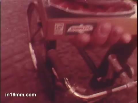 In this 16mm still from the Birdseye Frozen Parisian Vegetables commercial, a hand is shown holding a box of frozen vegetables, possibly in a lively, casual setting. The foreground features the handlebars of a bicycle, suggesting a playful or dynamic atmosphere. The focus is on promoting the convenience and appeal of Birdseye's frozen offerings. The overall imagery conveys a sense of everyday life while highlighting the product.