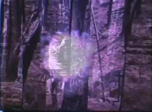 The 16mm still from the 'Showdown' trailer features a visually distressed image, likely depicting a scene in a forest setting. There's a notable purple hue, with a focus on an explosive or impactful moment, suggested by the bright glow. The graininess indicates it’s an older print, enhancing the nostalgic feel of the film.