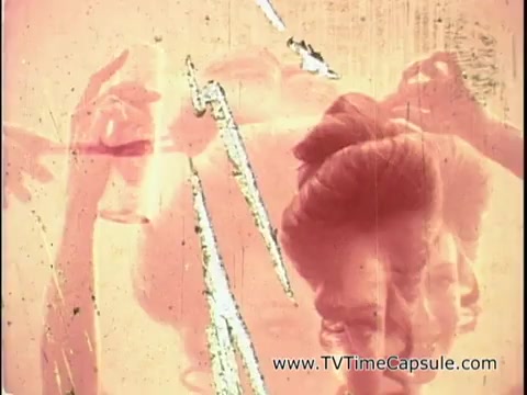 The still from the 16mm print of 'Adorn hairspray with kicky comb - 1970' features a close-up of a woman's hair being styled, likely showcasing the product's application. The image has a soft, faded quality typical of vintage film, with a warm color palette. The emphasis on the styling process aligns with the voiceover, promoting the effectiveness of Adorn hairspray and the complimentary kicky comb. Overall, it captures the essence of the era's beauty culture.