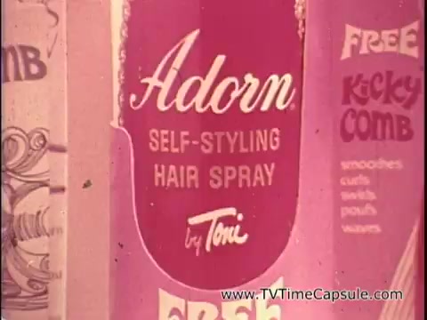 The still showcases a vibrant, retro advertisement for Adorn Self-Styling Hair Spray, prominently featuring the product name in a stylish script. The design emphasizes a fun and playful aesthetic typical of the 1970s, with bright colors and a focus on hair care. The text highlights a promotion for a free 'Kicky Comb,' suggesting additional styling benefits. Overall, the still captures the essence of hair fashion and self-styling from that era.
