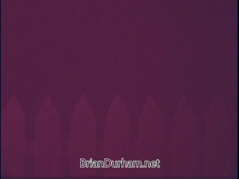 The still from 'Discover America PSA - 1969' features a simple composition with a solid purple background and a stylized fence or picket line along the bottom. The fence is shown in a lighter shade, creating a contrast with the vibrant background. The overall aesthetic is minimalistic, focusing on color and form rather than detailed imagery. The text at the center indicates a web address, likely related to the production or preservation of the PSA.