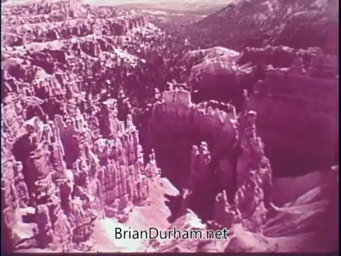 The still from the 'Discover America PSA - 1969' showcases a stunning aerial view of a rugged landscape, likely depicting the unique rock formations of Bryce Canyon. The scene features towering hoodoos and a vast expanse of trees, embodying the natural beauty and diverse geography of America, typical of promotional material aimed at encouraging tourism. The color tone appears to have a vintage look, aligned with the film's era.
