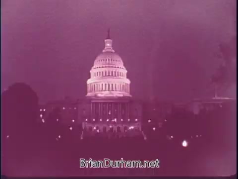 The still shows the United States Capitol building, illuminated against a twilight sky. The image has a purple tint, giving it a nostalgic feel, typical of mid-20th century film. The scene captures the grandeur of American architecture, likely intended to evoke a sense of pride and encourage exploration of the nation.
