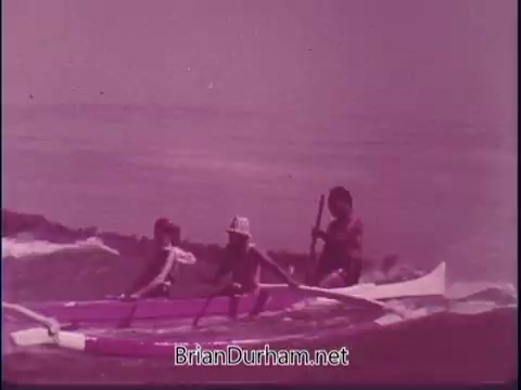 The still from the 1969 'Discover America' PSA shows a colorful beach scene with people on a canoe or kayak. There are two children paddling in the foreground, one wearing a hat. An adult or older figure is seen behind them, possibly steering. The overall tone of the image is warm, reflecting a vibrant outdoor activity.