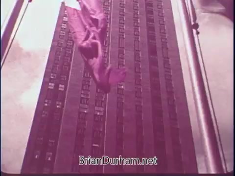 The still features an aerial view of a tall building, showcasing its architectural lines and windows. A purple cloth or fabric is draped over the structure, possibly as an artistic representation or symbol. The image has a vintage quality, consistent with its 1969 context as part of the 'Discover America' public service announcement, likely aiming to promote American landscapes or urban environments.