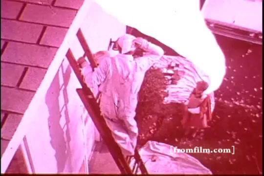 The still from the 'Ajax White Tornado' commercial shows a scene with a person on a ladder, seemingly cleaning or working on the side of a house, dressed in white. In the background, a child is present, and there is an eye-catching visual element resembling a swirling white tornado, likely a metaphor for the cleaning power of Ajax. The overall color tone hints at a vintage aesthetic typical of 16mm film.